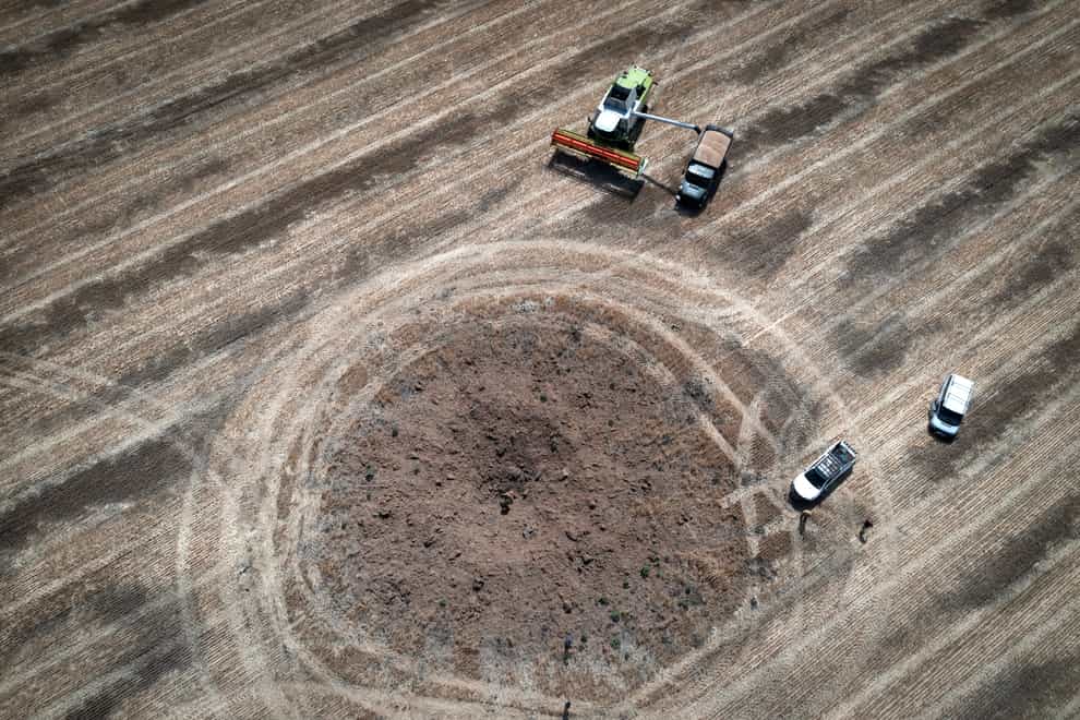 A farmer harvests crops round a crater left by a Russian rocket in his field in the Dnipropetrovsk region of Ukraine (Efrem Lukatsky/AP)