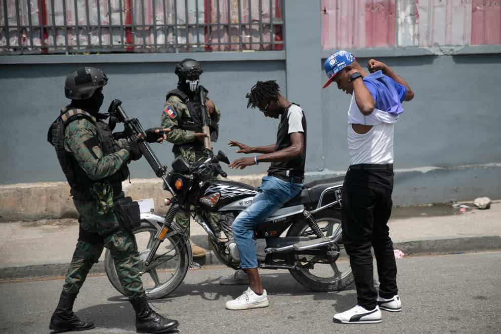 Armed forces check two men who were riding a motorcycle for weapons (Odelyn Joseph/AP)