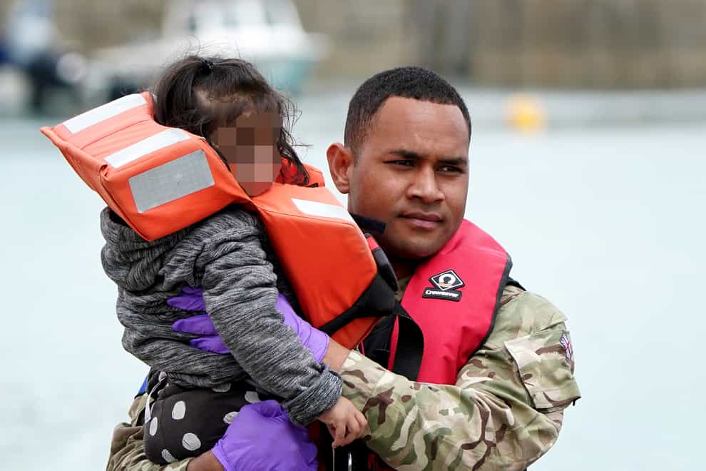 A young child is carried by a military officer as a group of people thought to be migrants are brought in to Dover, Kent, following a small boat incident in the Channel (Gareth Fuller/PA)