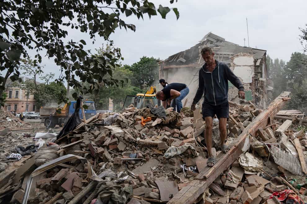 Local residents search for documents of their injured friend in the debris of a destroyed apartment house after Russian shelling in a residential area in Chuhuiv, Kharkiv region (AP)