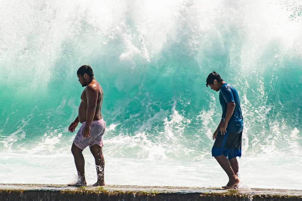 People walk in front of the high surf near Kapahulu Groin in Waikiki, Hawaii (Craig T. Kojima/Honolulu Star-Advertiser via AP)