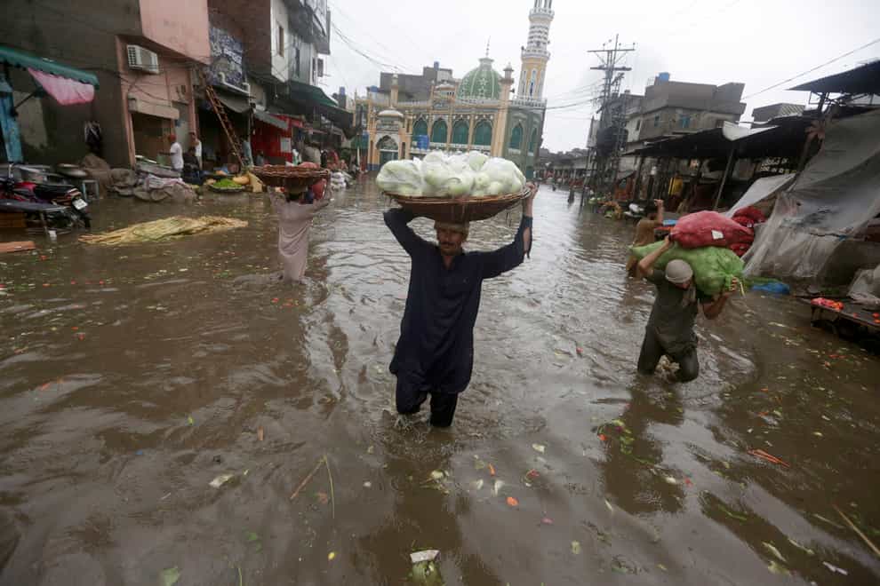 Labourers carry produce as they wade through a flooded road after heavy rainfall, in Lahore, Pakistan, Thursday, July 21, 2022 (KM Chaudary/AP/PA)