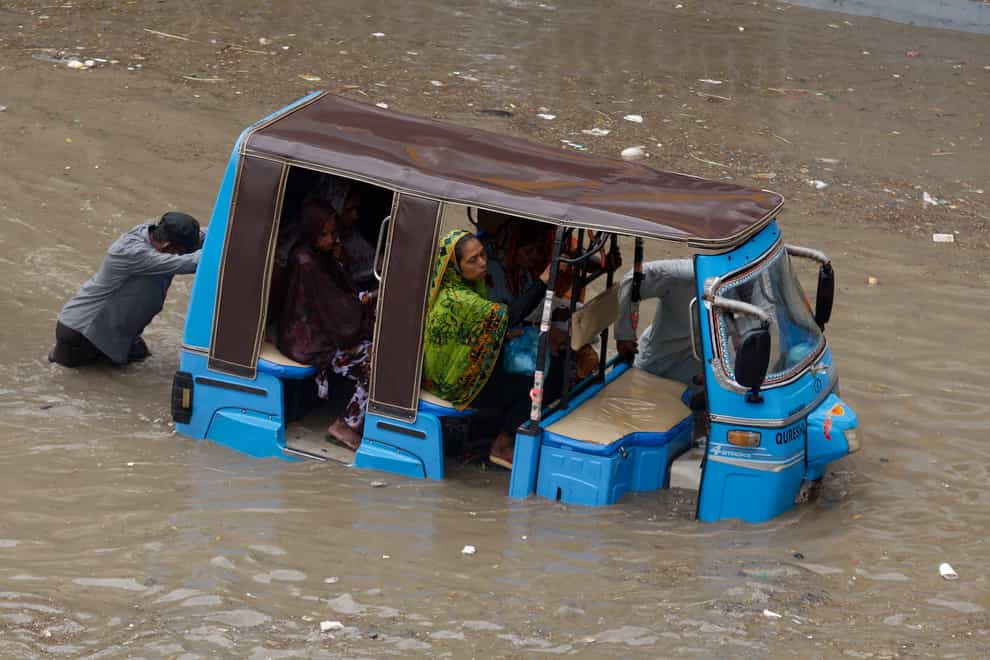 A rickshaw driver and a volunteer push a rickshaw stuck in a flooded road after a heavy rainfall in Karachi (AP)