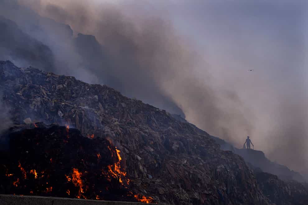 A person picks through trash for reusable items as a fire rages at the Bhalswa landfill in New Delhi, April 27, 2022. Landfills are releasing far more planet-warming methane into the atmosphere from the decomposition of waste than previously thought, a study suggests (Manish Swarup/AP/PA)