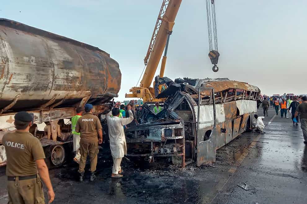 Police officers and workers remove the wreckage of a bus that collided with an oil tanker along a highway in Uch Sharif near Multan, Pakistan, Tuesday, Aug. 16, 2022 (AP/PA)