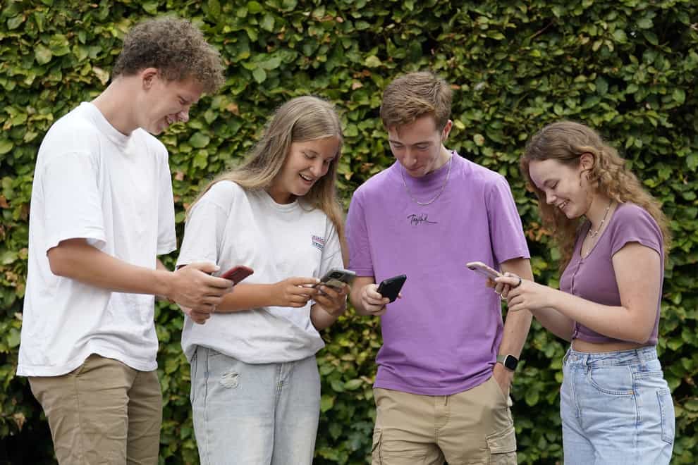 Students Ben Surtees, Bryony Lucas, James McSaprron and Leonie Rowe check their results on their phones at Peter Symonds College, Winchester, Hampshire (Andrew Matthews/PA)