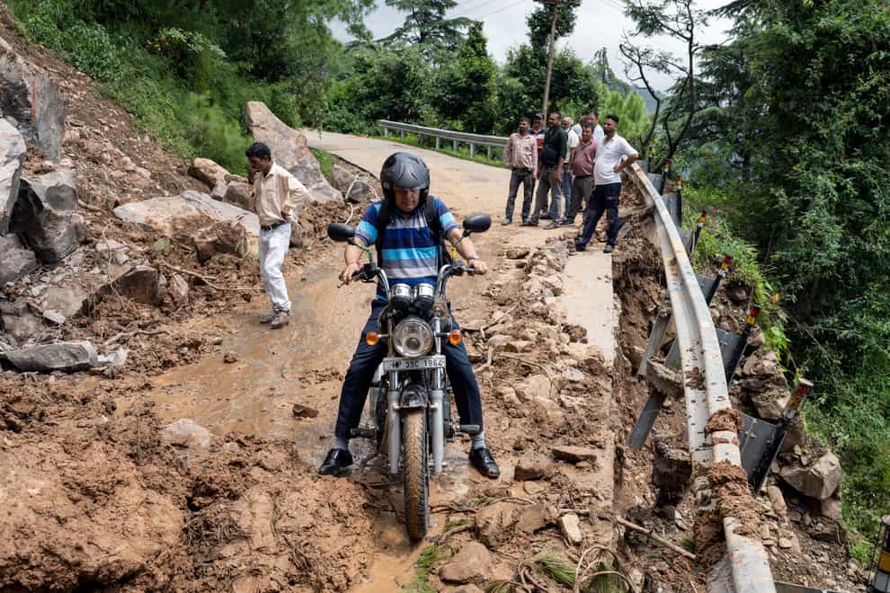 A motorcyclist tries to drive past mud and debris after a landslide hit a road in Dharmsala, Himachal Pradesh state (Ashwini Bhatia/AP)