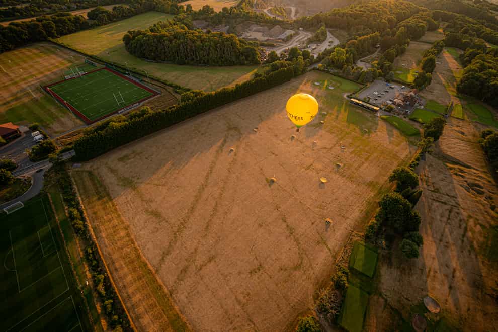 A hot air balloon flies over a browning and parched golf driving range in Somerset (Ben Birchall/PA)