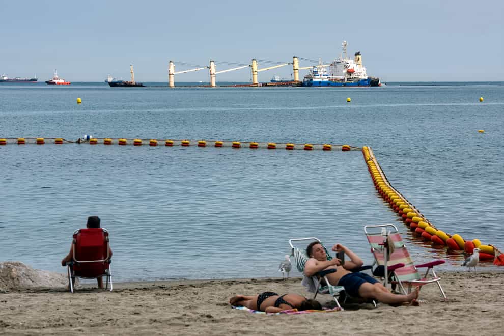 People relax on a beach in front of the stricken Tuvalu-registered OS 35 cargo ship that collided with a liquid natural gas carrier in the bay of Gibraltar (Marcos Moreno/AP)