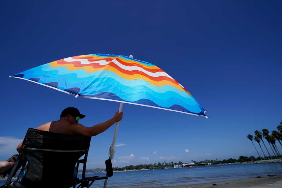 A man sits under a shade in Mission Bay, California (Gregory Bull/AP)