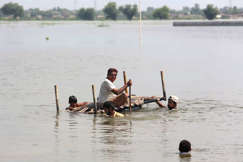People use a makeshift raft to try and salvage belongings from their nearby flooded homes (Fareed Khan/AP)