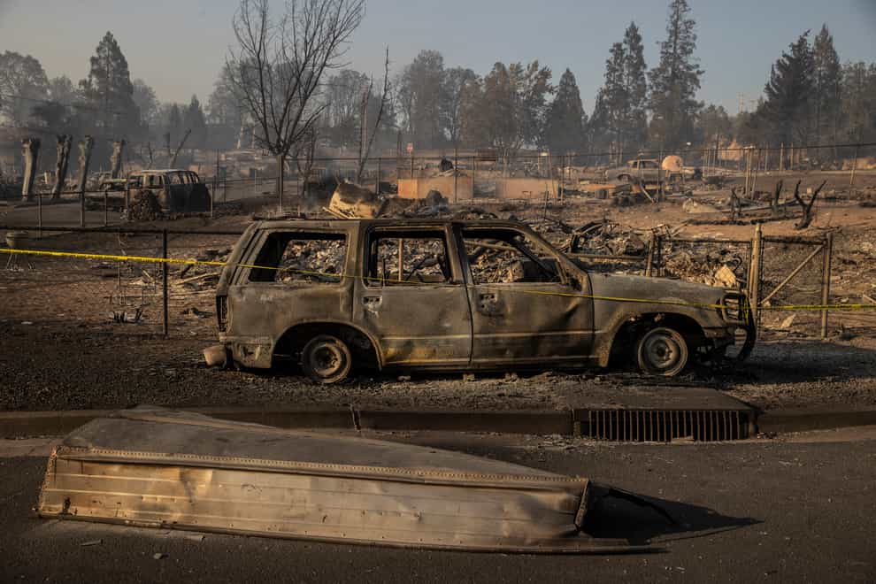 A boat is seen on a road in front of a burned vehicle in the Lincoln Heights neighbourhood during the Mill Fire in Weed (Stephen Lam/AP)