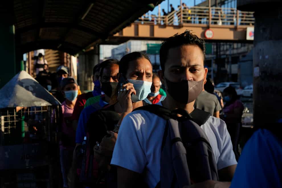 Commuters wearing face masks wait for a ride at a bus stop in Manila, Philippines (Aaron Favila/AP)
