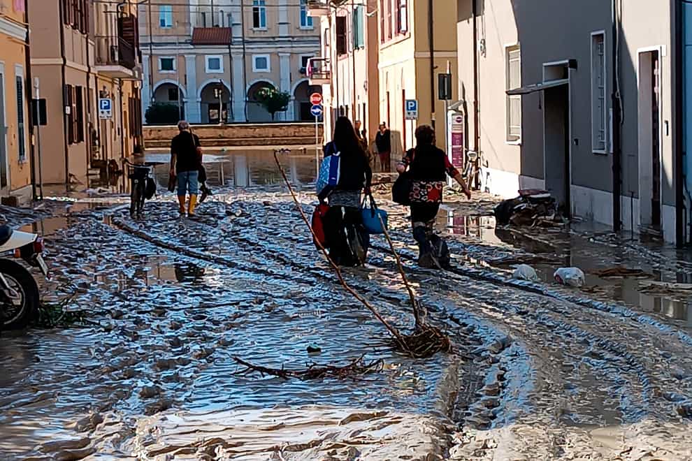 People walk on mud and debris in Senigallia, Italy (Gabriele Moroni/LaPresse via AP)