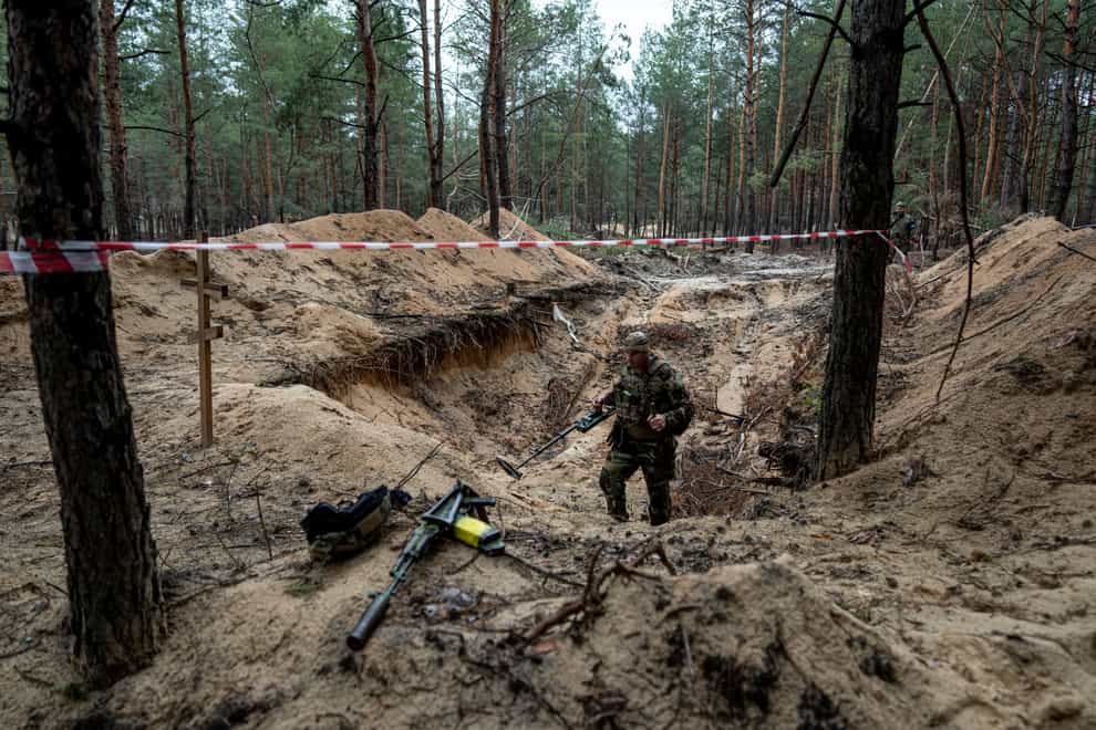 A Ukrainian serviceman uses a metal detector to inspect a mass grave in Izium (Evgeniy Maloletka/AP)