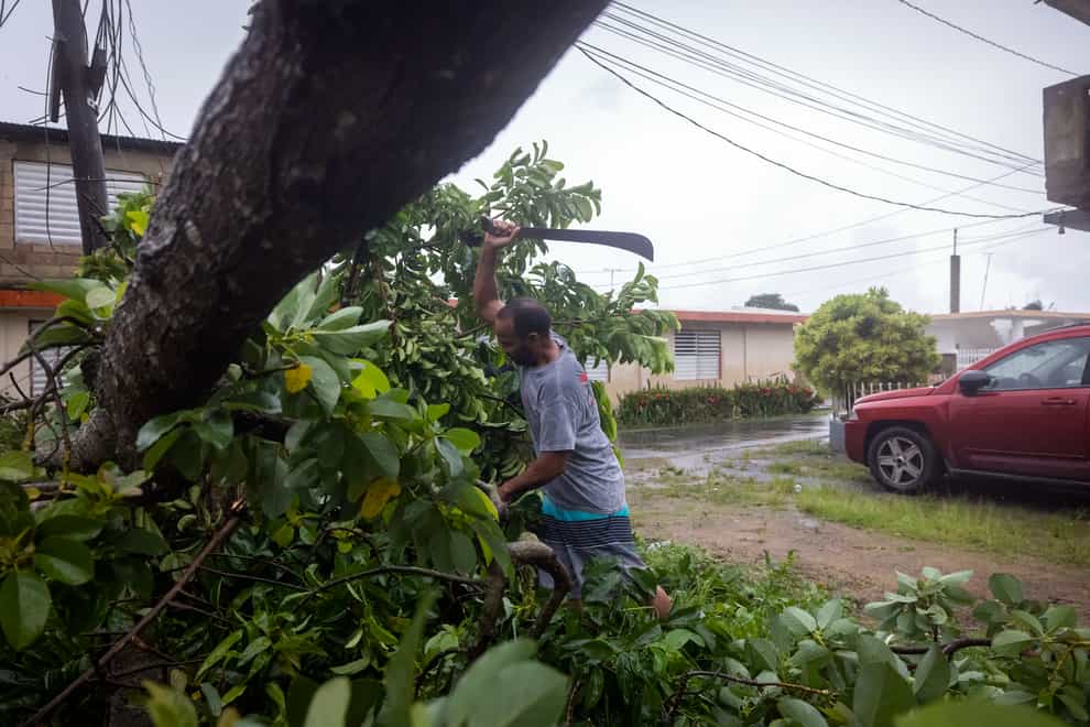 A man uses a machete to cut a tree that was felled by the wind from Hurricane Fiona in Loiza, Puerto Rico, Monday, Sept. 19, 2022. (AP Photo/Alejandro Granadillo)