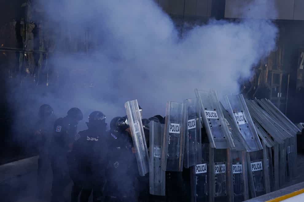 Police officers take cover behind a shield wall during clashes with demonstrators (Fernando Llano/AP)