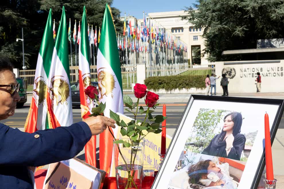 A person places a flower in front of a portrait of Masha Amini during a protest rally in front of the European headquarters of the United Nations in Geneva (Keystone via AP)