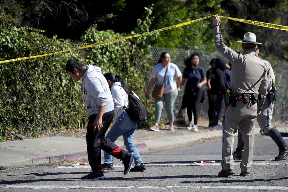 A California Highway Patrol officer lifts police tape to let parents and students leave a cordoned off area in Fountain Street following a shooting at a school campus in Oakland (Ray Chavez/Bay Area News Group/AP)