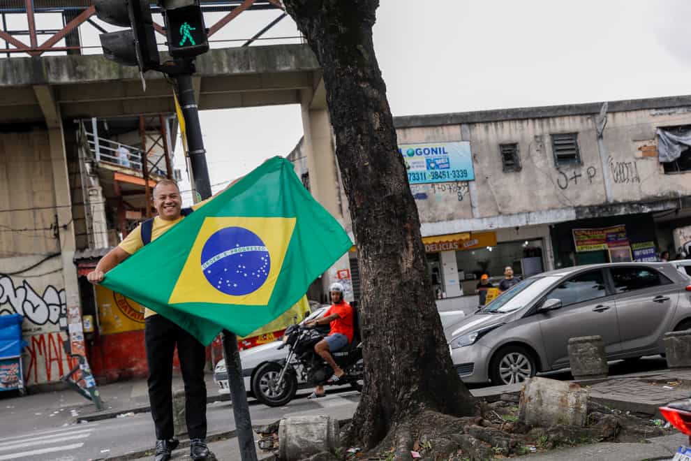 A supporter of Brazilian President Jair Bolsonaro, who is running for another term, displays his country’s flag as he waits to see him drive thru outside the polling station where he voted in Rio de Janeiro, Brazil, Sunday, Oct. 2, 2022. (AP Photo/Bruna Prado)