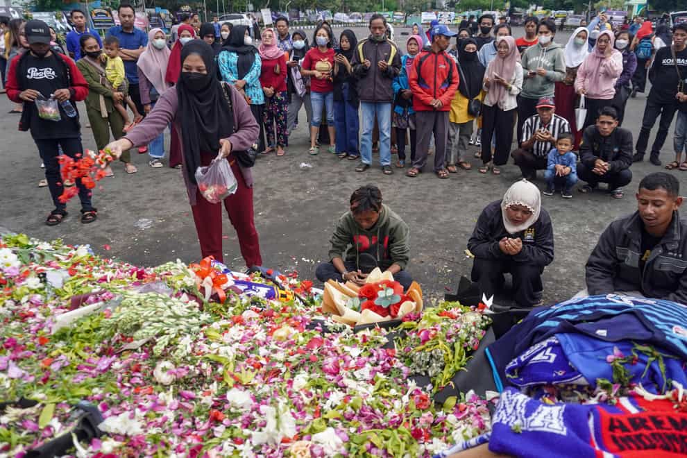 A woman throws flowers as she and others offer prayers for the victims of the soccer stampede outside the Kanjuruhan Stadium in Malang, East Java, Indonesia (Dicky Bisinglasi/AP/PA)