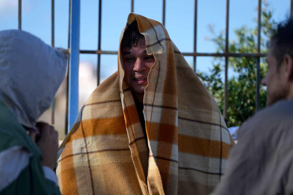 An Afghan covered with a blanket, speaks with other migrants at an old school used as a temporary shelter on the island of Kythira, southern Greece, Friday, Oct. 7, 2022. Strong winds were hampering rescue efforts at two Greek islands Friday for at least 10 migrants believed to be missing after shipwrecks left more than 20 people dead, officials said (Thanassis Stavrakis/AP/PA)