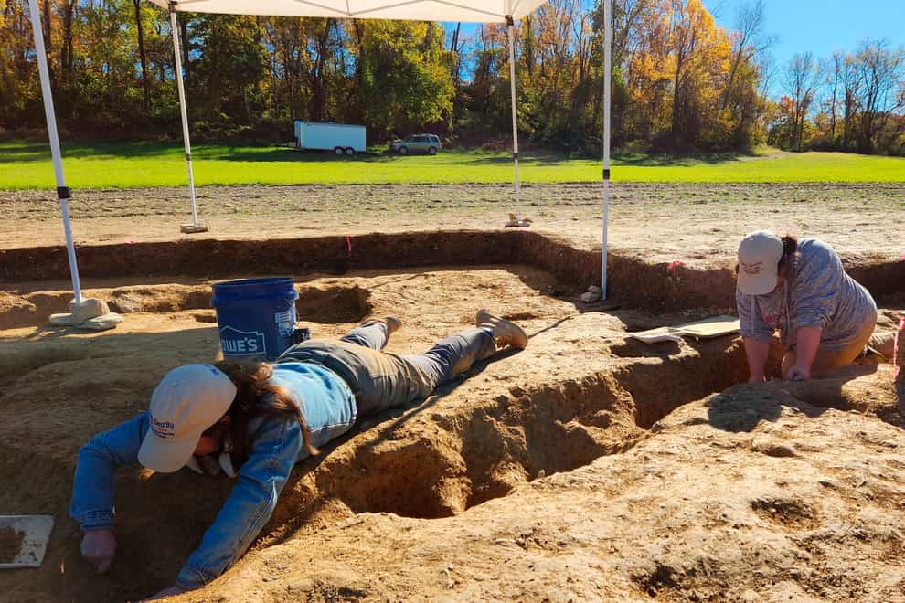 Jane C Skinner and Samantha Muscella excavate post holes at the bottom of a stockade trench (John Crawmer via AP)