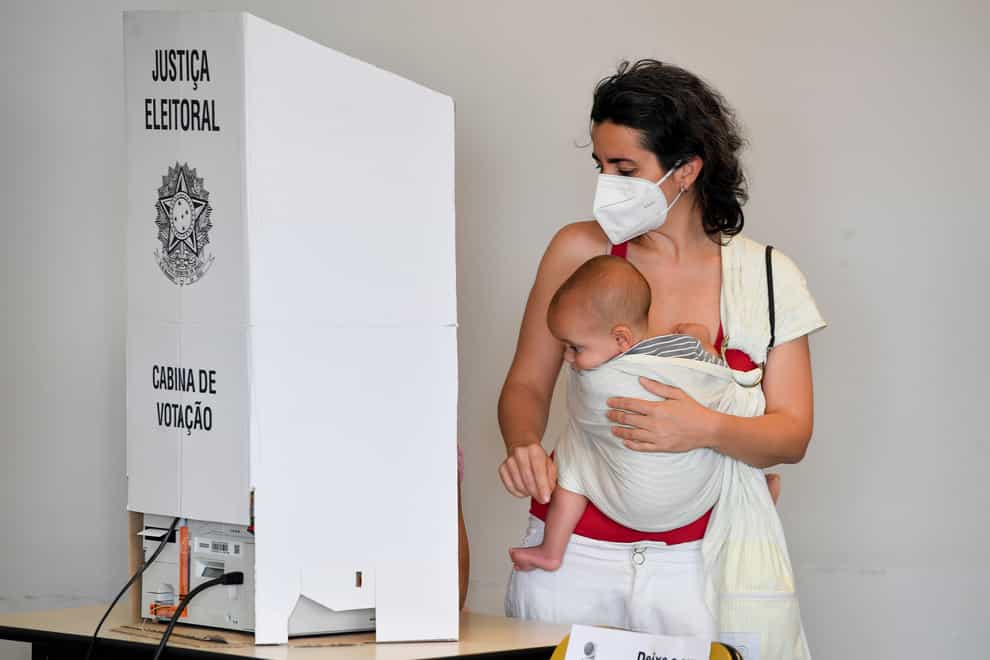 A woman votes while holding a baby during the presidential run-off election in Sao Pablo (Matias Delacroix/AP)