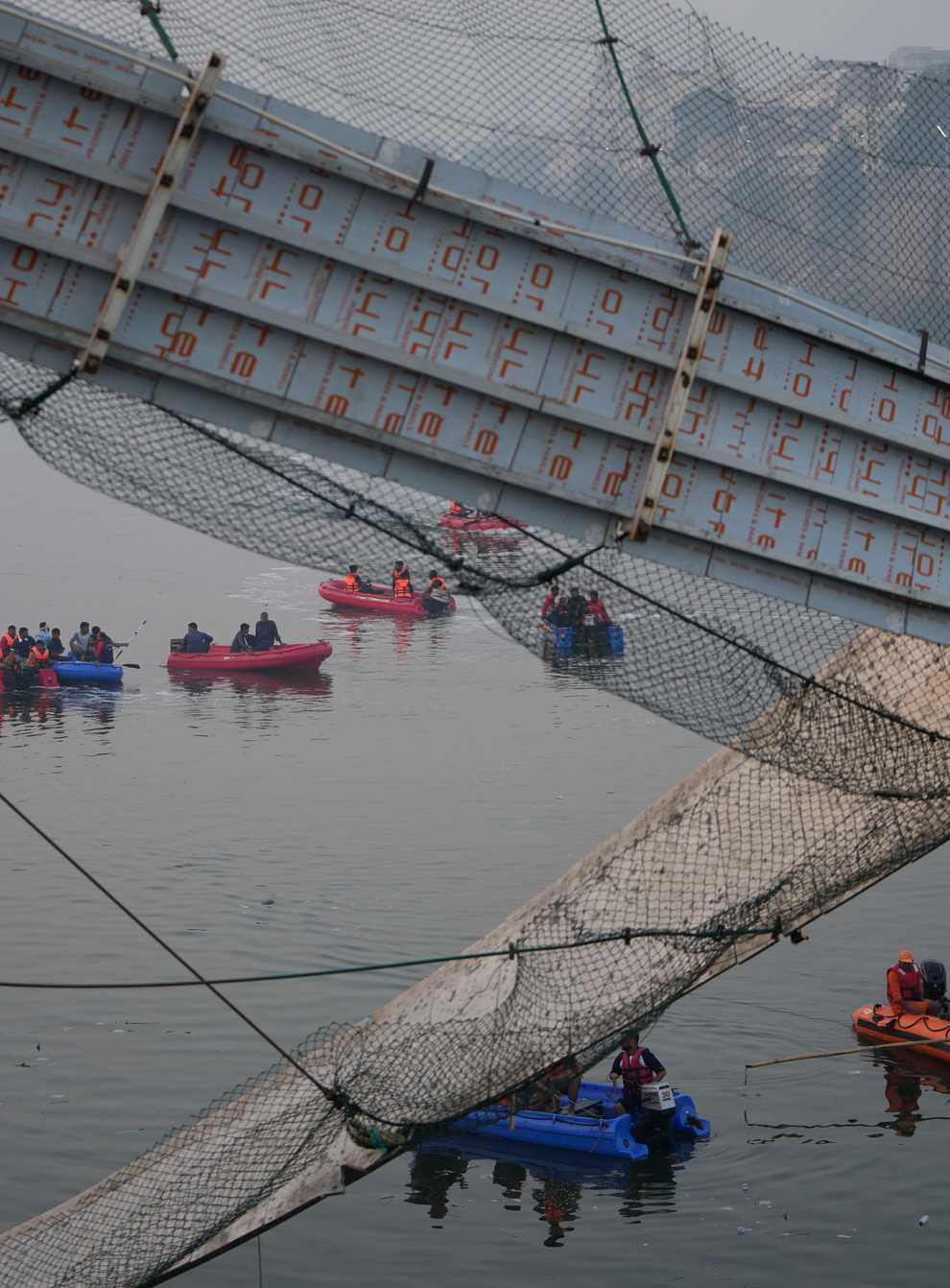 Rescuers on boats search in the Machchu river next to a cable suspension bridge that collapsed in Morbi town of western state Gujarat, India (Ajit Solanki/AP)