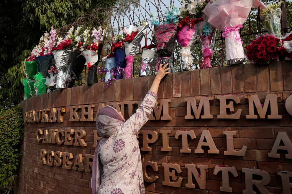 A woman places a bouquet over the wall of a hospital where former Pakistani prime minister Imran Khan is being treated for a gunshot wound in Lahore, Pakistan (KM Chaudhry/AP)
