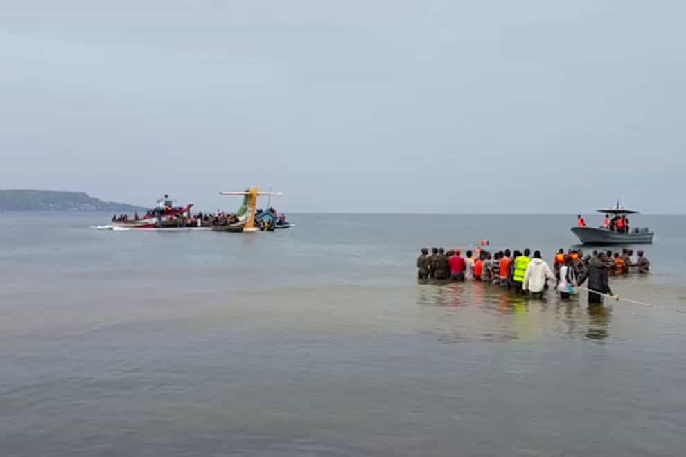 Rescuers near the tail fin of a crashed aircraft on the shores of Lake Victoria in Bukoba, western Tanzania (AYO TV via AP)