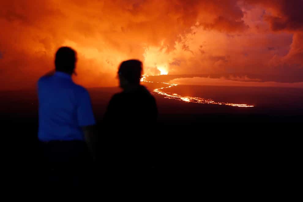 Spectators watch the lava flow down the mountain from the Mauna Loa eruption (AP)