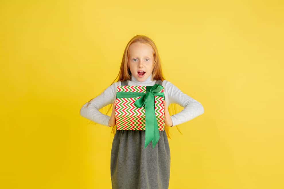 2D9EMGG Giving and getting presents on Christmas holidays. Teen smiling girl having fun, holding big gifts isolated on yellow studio background. New Year 2021 meeting, childhood, happiness, emotions.