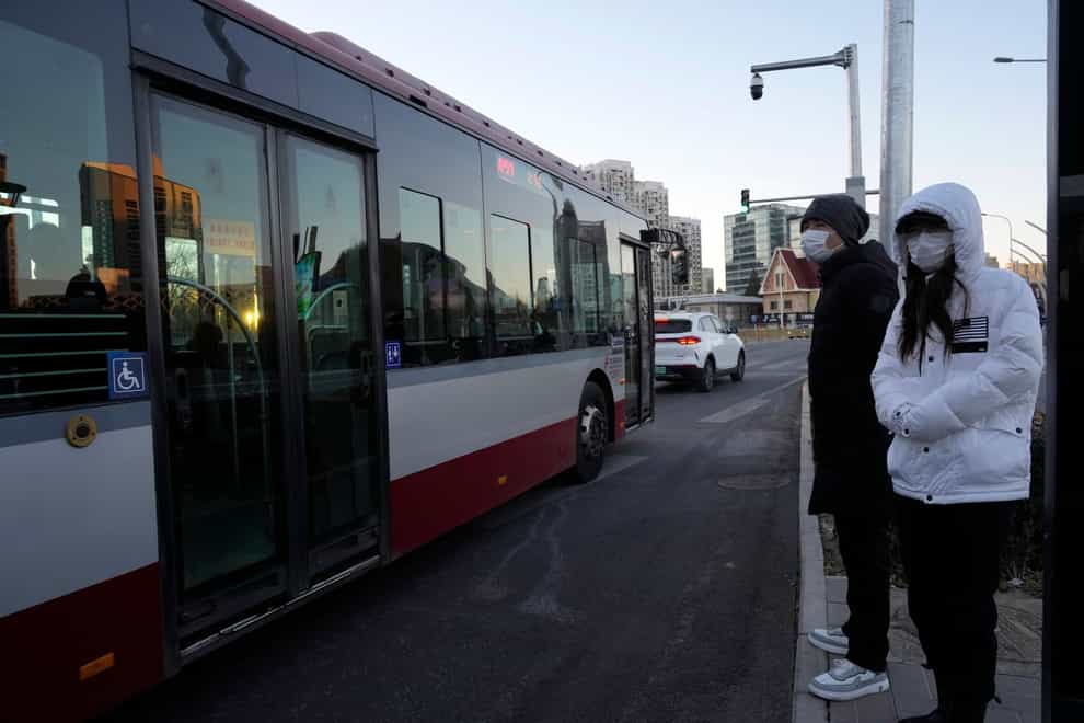 Residents wearing masks wait at a public bus stop in Beijing (Ng Han Guan/AP)