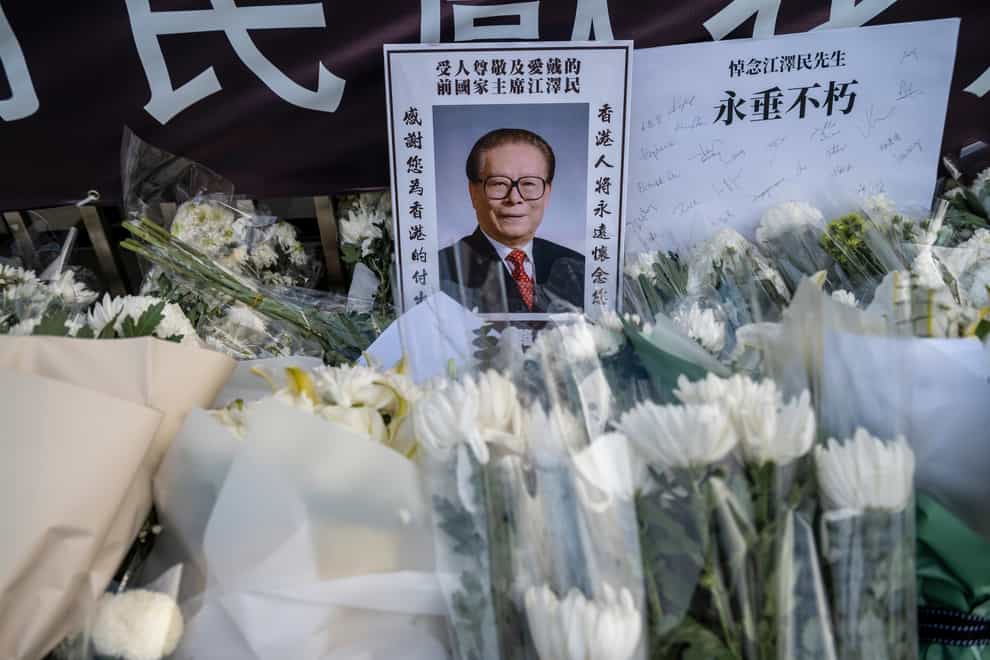 A photo of the late former Chinese President Jiang Zemin is placed amongst flowers and the word ‘Immortal’ outside the Liaison Office in Hong Kong (AP)