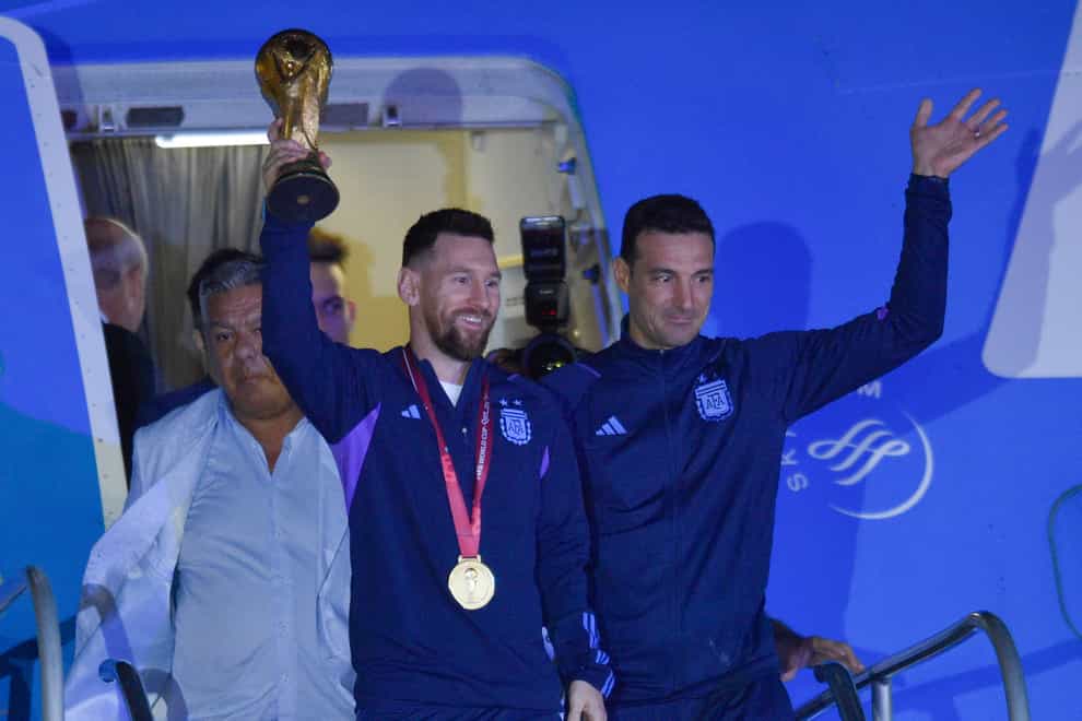 Argentina’s Lionel Messi holds the World Cup trophy as he leaves the plane (Gustavo Garello/AP)