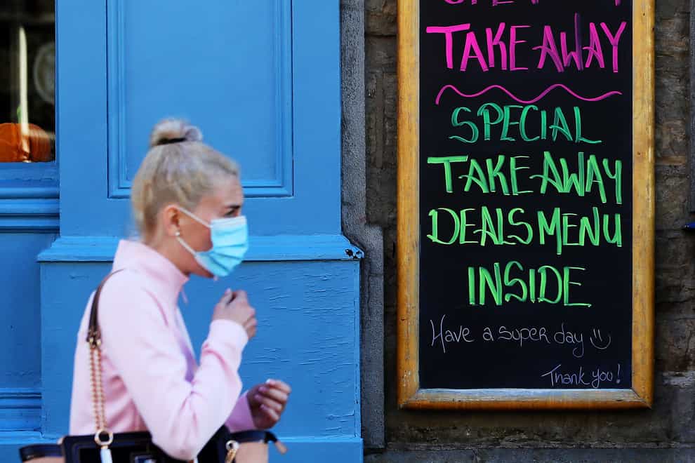 A woman wearing a face mask walks past a sign outside a cafe on a street in Co Cavan (PA)