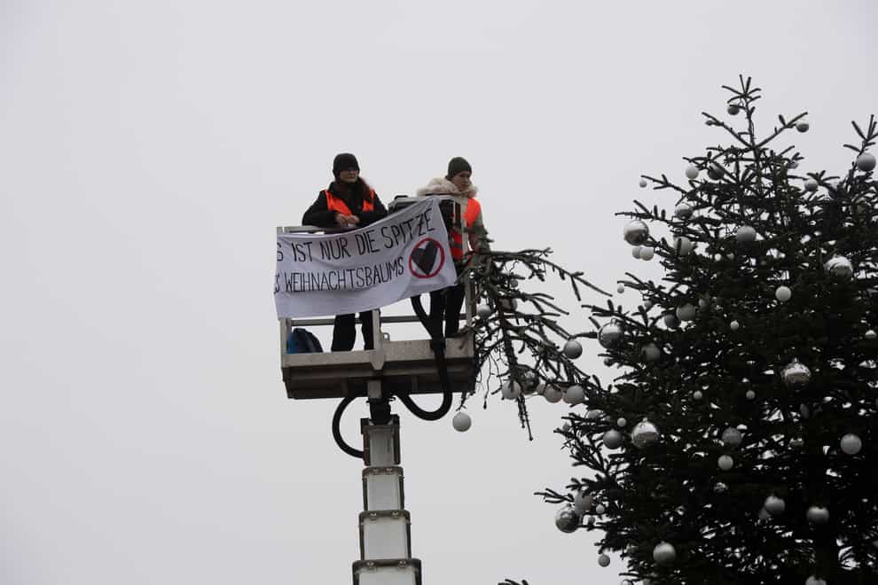 Activists hold the top of a Christmas Tree and show a banner reading: ‘It’s just the top of the Christmas tree’ at the Pariser Platz in Berlin, Germany (Paul Zinken/dpa/AP)