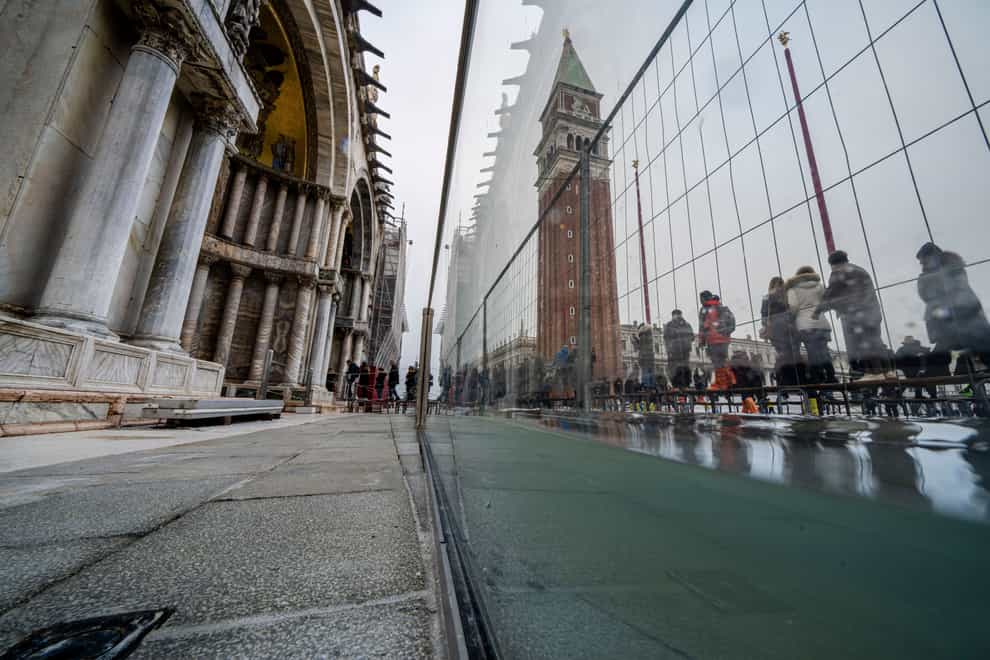 Tourists and residents use walkways to cross a flooded St Mark’s Square in Venice, where recently installed glass barriers prevent seawater from flooding the 900-year-old basilica (Domenico Stinellis/AP)