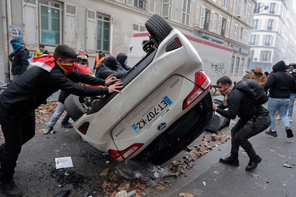 Demonstrators turn over a car during the protest (Lewis Joly/AP)