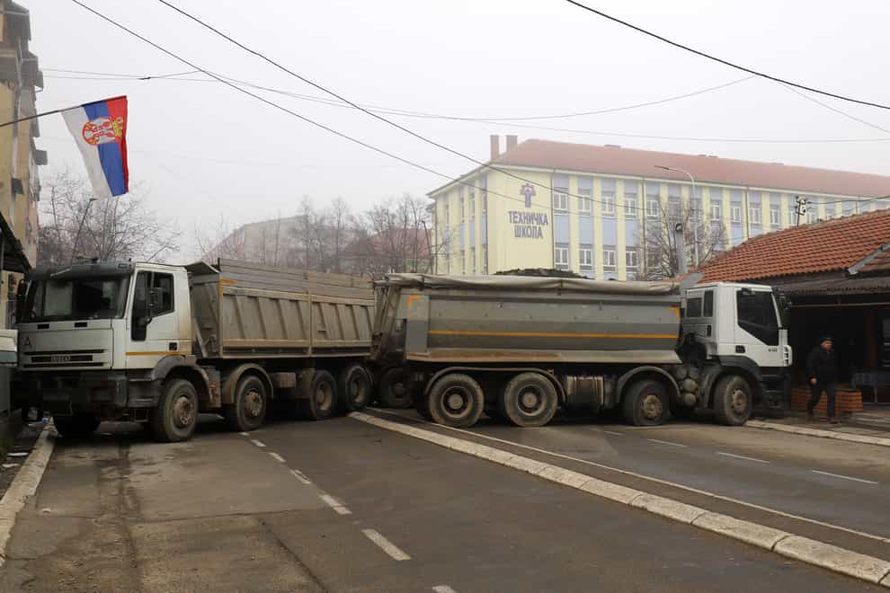 A man passes by a barricade made of trucks loaded with stones that was erected during the night on a street in northern, Serb-dominated part of ethnically divided town of Mitrovica, Kosovo, Tuesday, Dec. 27, 2022. Serbia on Monday placed its security troops on the border with Kosovo on “the full state of combat readiness,” ignoring NATO’s calls for calming down of tensions between the two wartime Balkan foes. (AP Photo/Bojan Slavkovic)