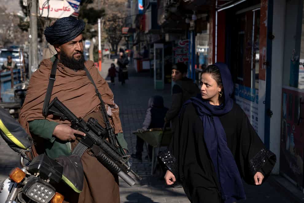 A Taliban fighter stands guard as a woman walks past in Kabul, Afghanistan (Ebrahim Noroozi/AP)
