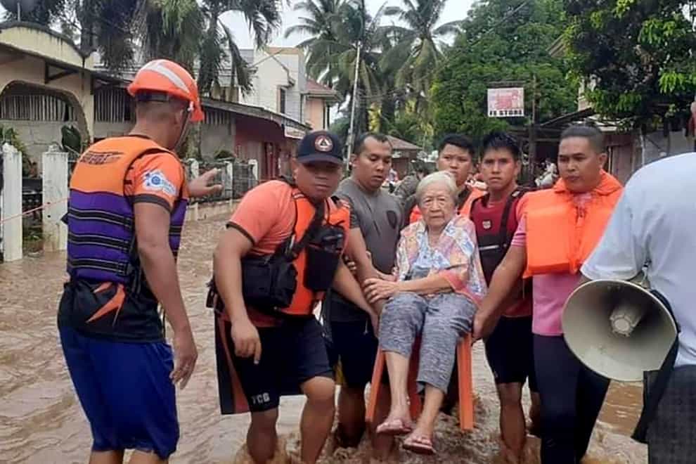 An elderly woman sits on a chair while being carried by coast guard personnel wading through floodwaters in Plaridel, Misamis Occidental province in the southern Philippines (Philippine Coast Guard via AP/PA)
