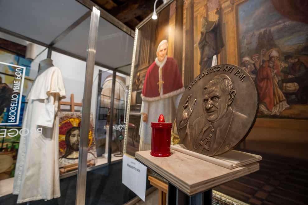 A metal disc shows Pope Emeritus Benedict XVI alongside a painting of him and one of the last cassocks worn by him before his resignation in 2013, according to the director of the Progetto Arte Poli gallery where it is displayed, near the Vatican (Ben Curtis/AP)