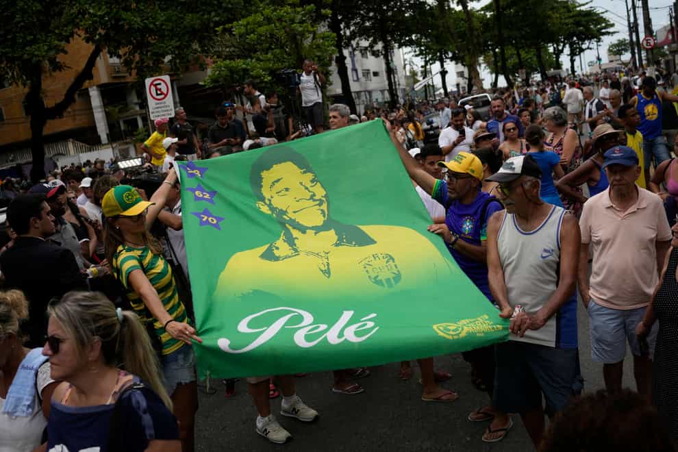 People hold a banner of the late Brazilian football great Pele along the route of his funeral procession from Vila Belmiro stadium to the cemetery in Santos, Brazil (Matias Delacroix/AP)
