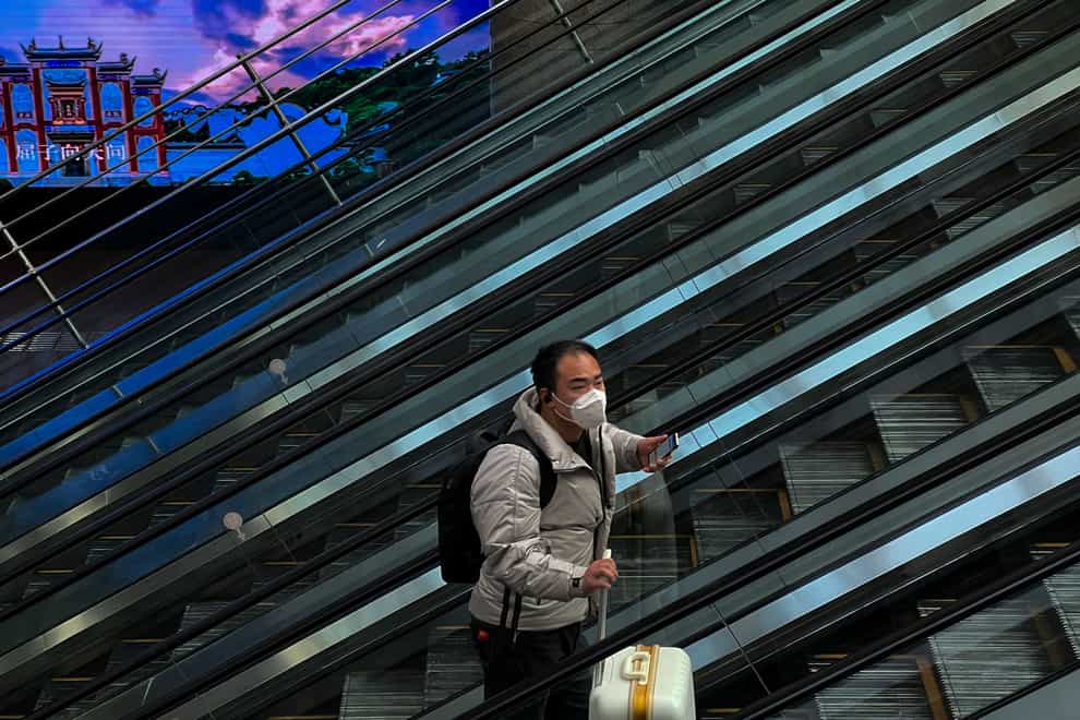 A man wearing a face mask with his luggage moves on an escalator at the West Railway Station in Beijing (Wayne Zhang/AP)