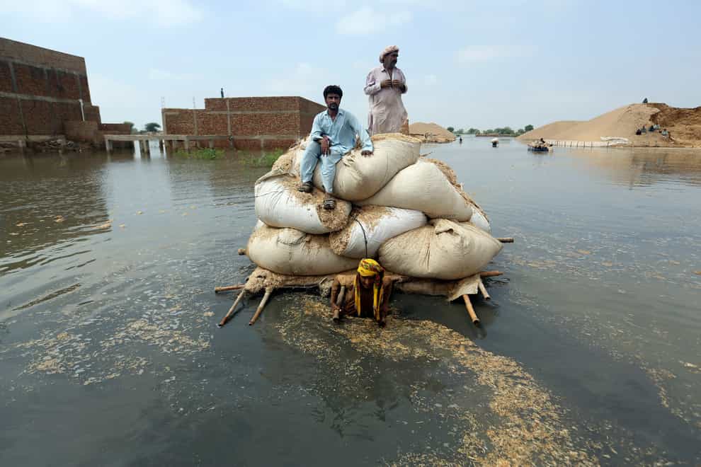 Flood victims use a makeshift barge to carry hay for cattle in Jaffarabad, a district of Pakistan’s southwestern Baluchistan province, in September 2022 (Fareed Khan/AP)