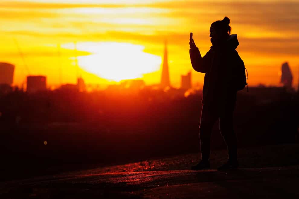 A woman takes a photograph of the sunrise from Primrose Hill in west London during a cold and frosty morning (Victoria Jones/PA)