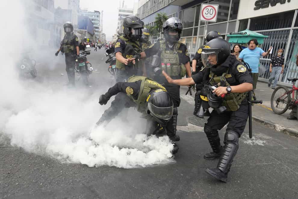Police officers pick up a tear gas canister that was thrown back at them by anti-government protesters who travelled to the capital from across the country to march against Peruvian President Dina Boluarte in Lima, Peru(Martin Mejia/AP/PA)