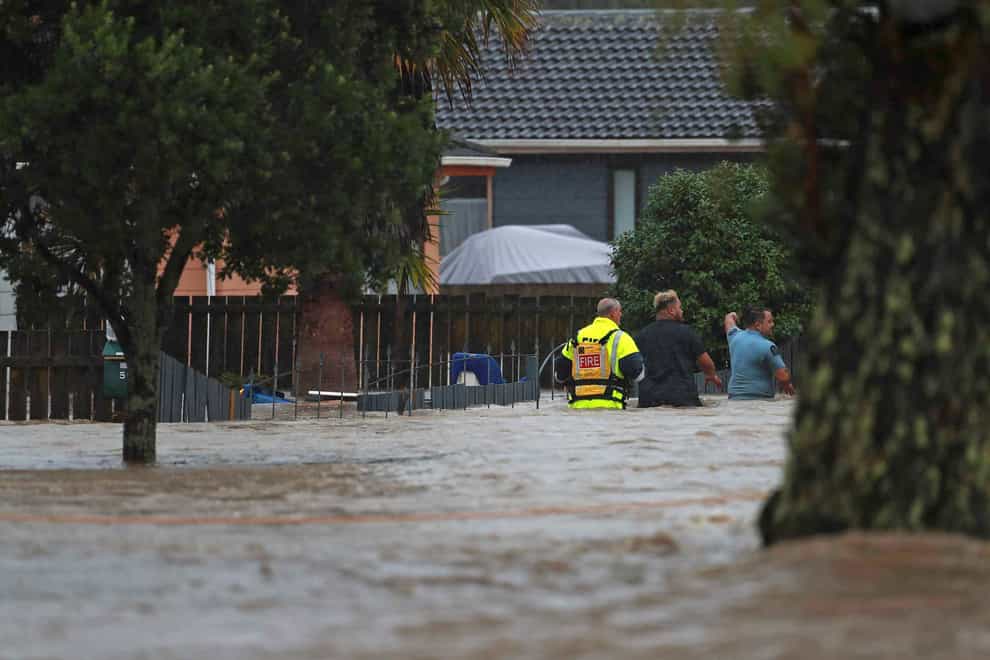 Emergency workers and a man wade through floodwaters in Auckland, New Zealand (Hayden Woodward/New Zealand Herald via AP)
